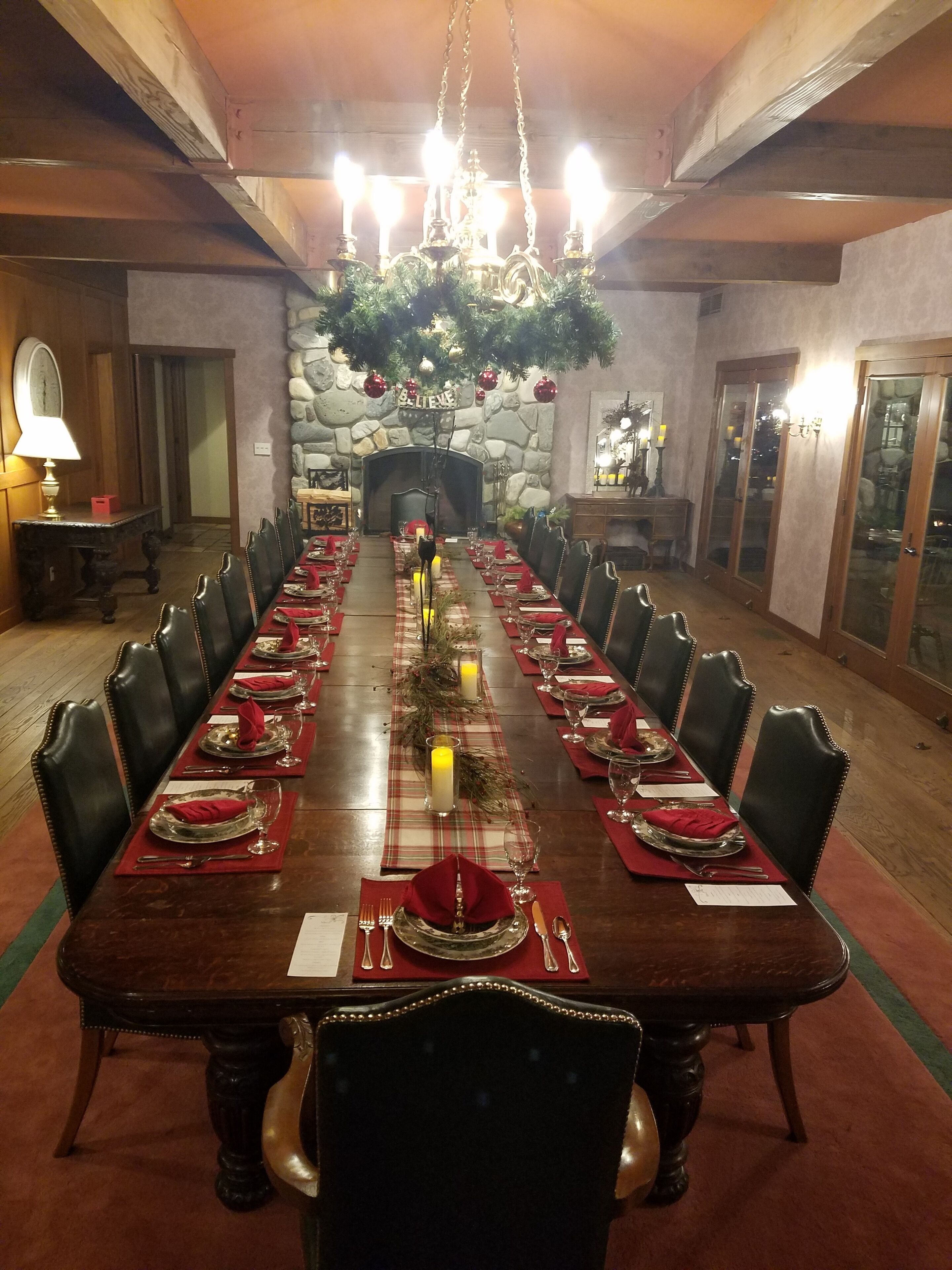 A long dining table set for a formal meal with chairs, candles, and a fireplace in the background.