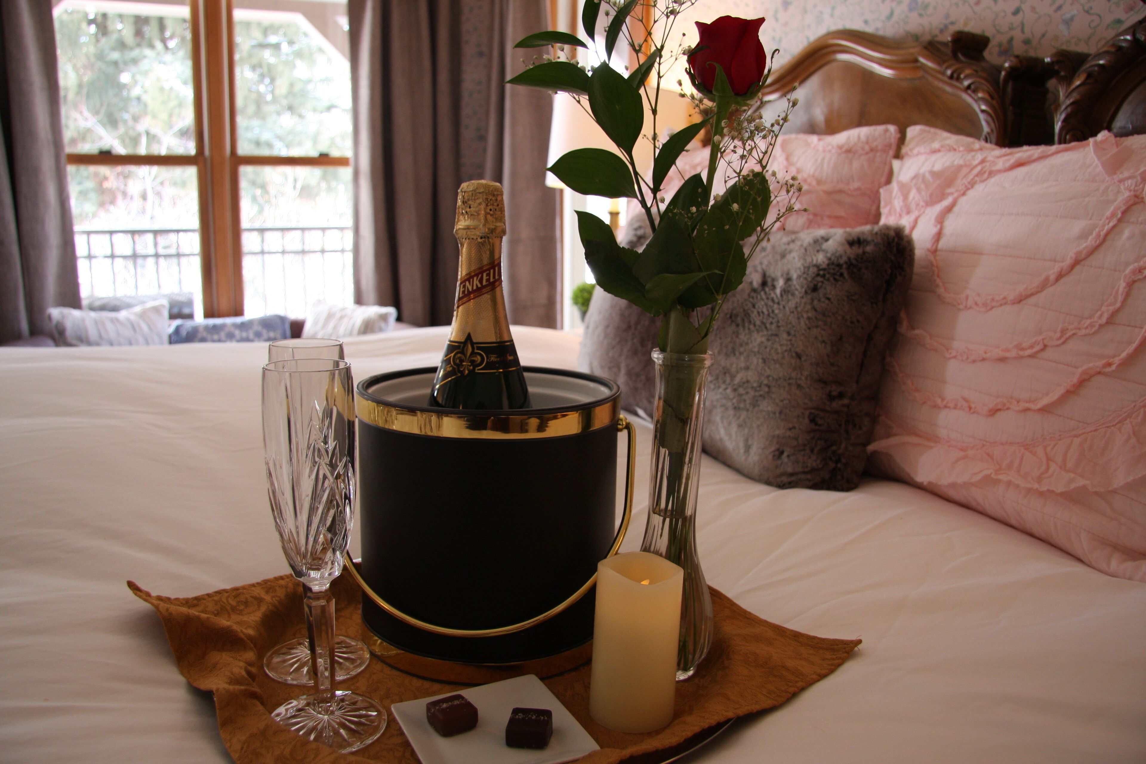 A bed with a champagne bucket, two glasses, a candle, and a vase with a rose.