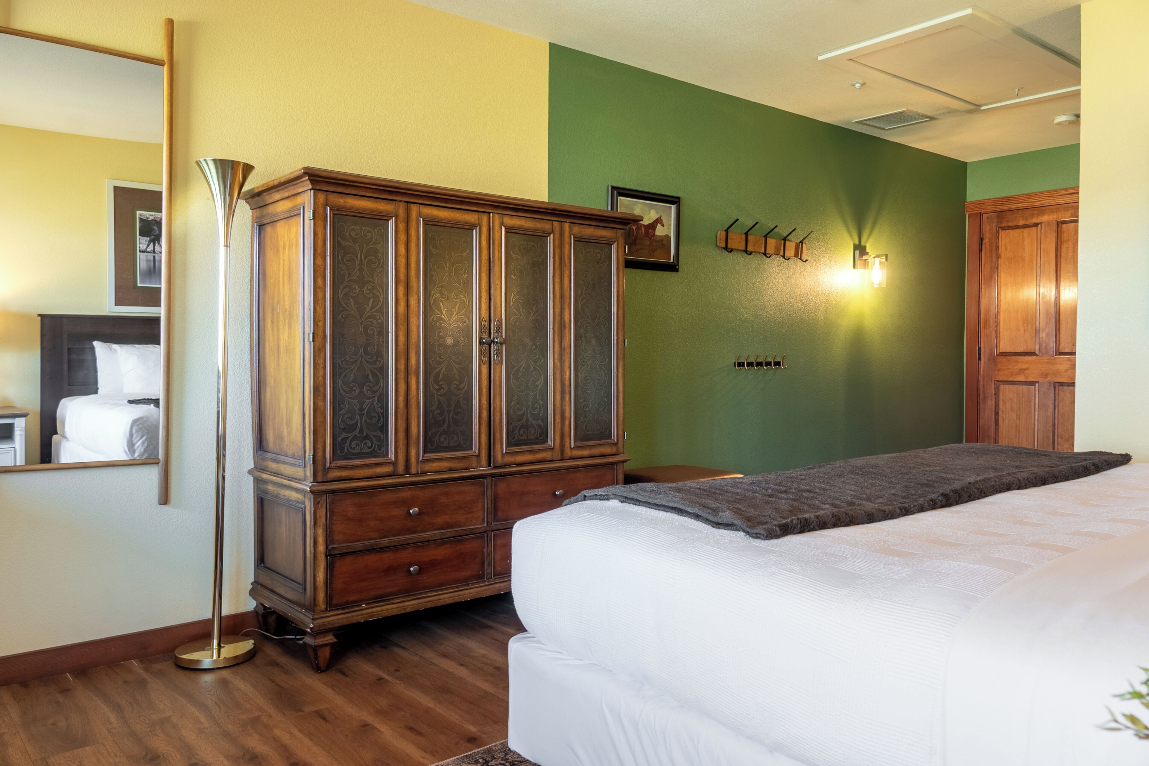 Une chambre à coucher comprenant un lit, une armoire en bois, une lampe sur pied, un luminaire fixé au mur et un tableau représentant un cheval.