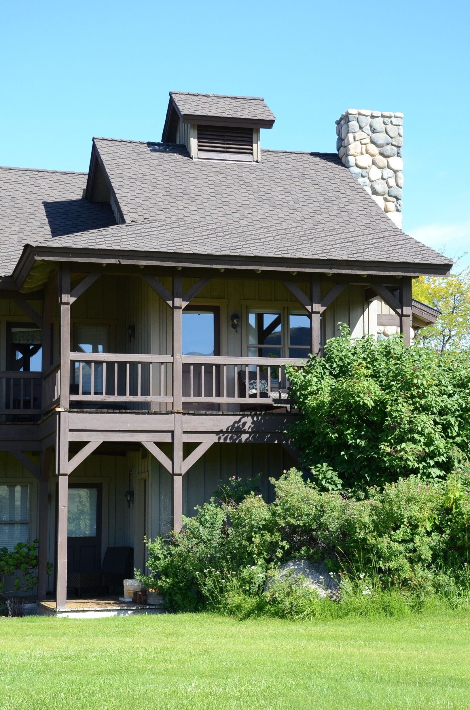 A two-story house with a stone chimney, a balcony, and a well-maintained lawn.