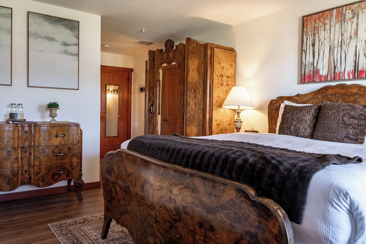 A bedroom with a wooden bed, a nightstand, a dresser, and a painting on the wall.