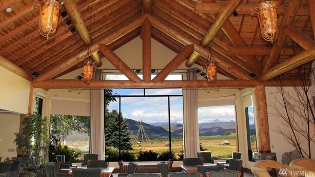 A spacious room with a high wooden ceiling and large windows offering a view of mountains and a teepee.
