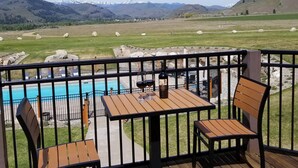 A deck with wooden furniture overlooking a pool and a scenic view of mountains and fields.