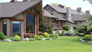 A large, modern house with a spacious front yard, stone chimneys, and a well-maintained garden.