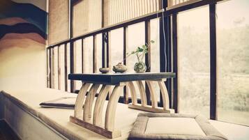 A room with a wooden bench, a small table with decorative items, and a view through large windows.