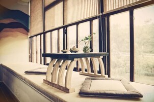 Una habitación con un banco de madera, una mesita con objetos decorativos y vistas amplias a través de grandes ventanales.