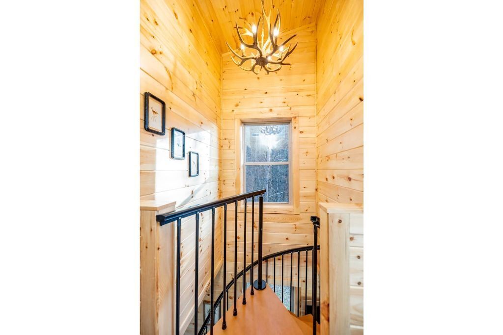Interior de madera con una escalera, una araña y un ventanal.