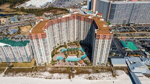 A high-rise hotel with a central courtyard featuring a swimming pool and palm trees. - Shores of Panama 926- Free Beach Chairs! (Panama City Beach)