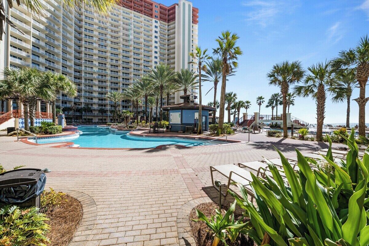 A hotel pool area with a large pool, palm trees, and a building in the background.
