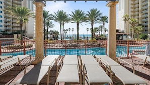 A pool area with lounge chairs, palm trees, and a view of the ocean. - Shores of Panama 926- Free Beach Chairs! (Panama City Beach)