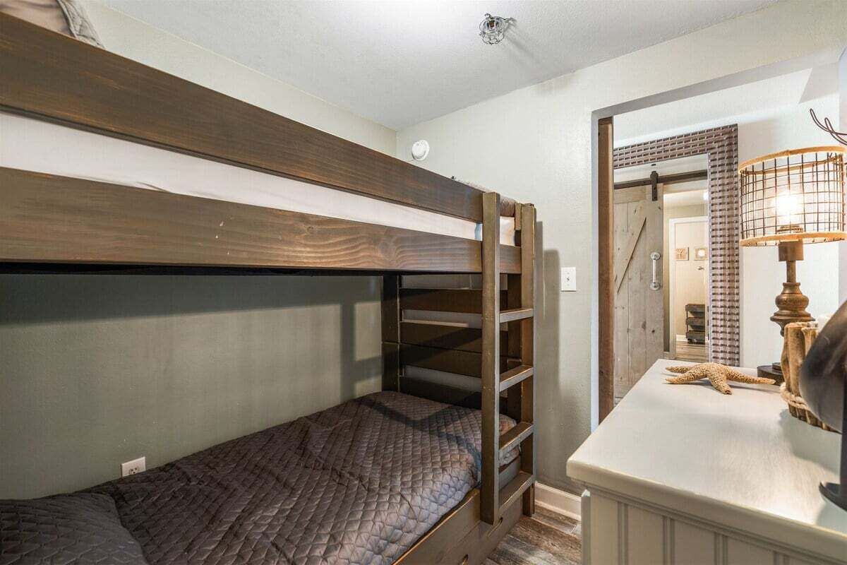 A bunk bed with a quilted mattress, a wooden headboard, and a small desk with a lamp and starfish decoration.