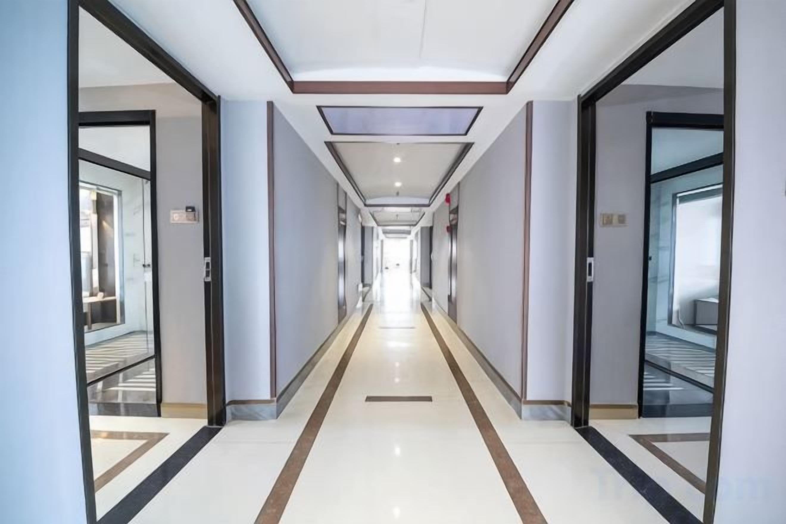 A long, narrow hotel corridor with doors on both sides leading to rooms.