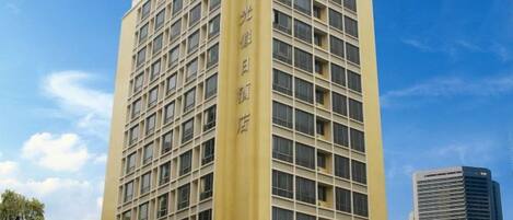 Un hôtel à plusieurs étages, avec une façade jaune et un ciel bleu clair en arrière-plan.