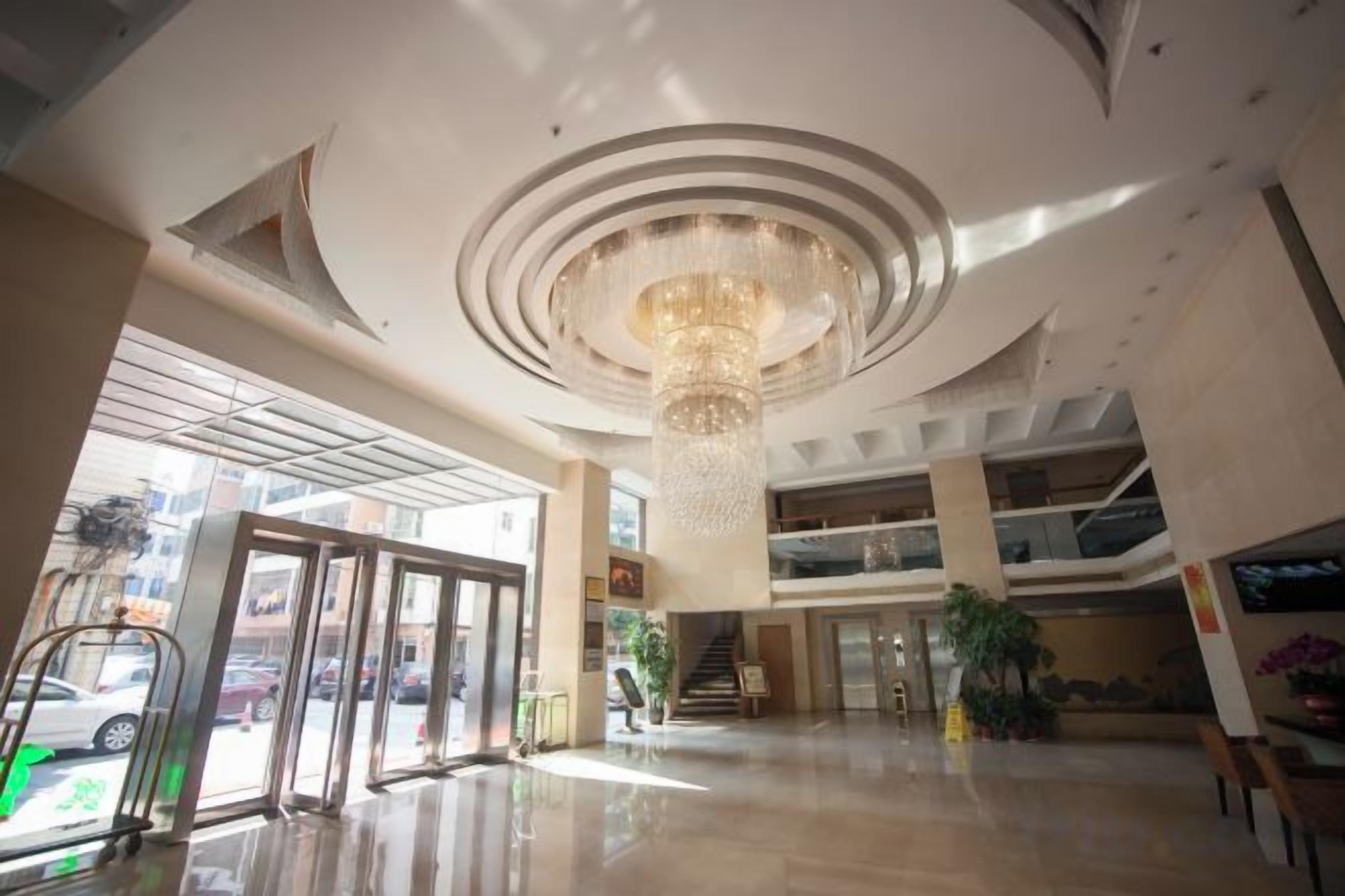 A spacious lobby with a large chandelier, a glass entrance, and a staircase leading to upper floors.