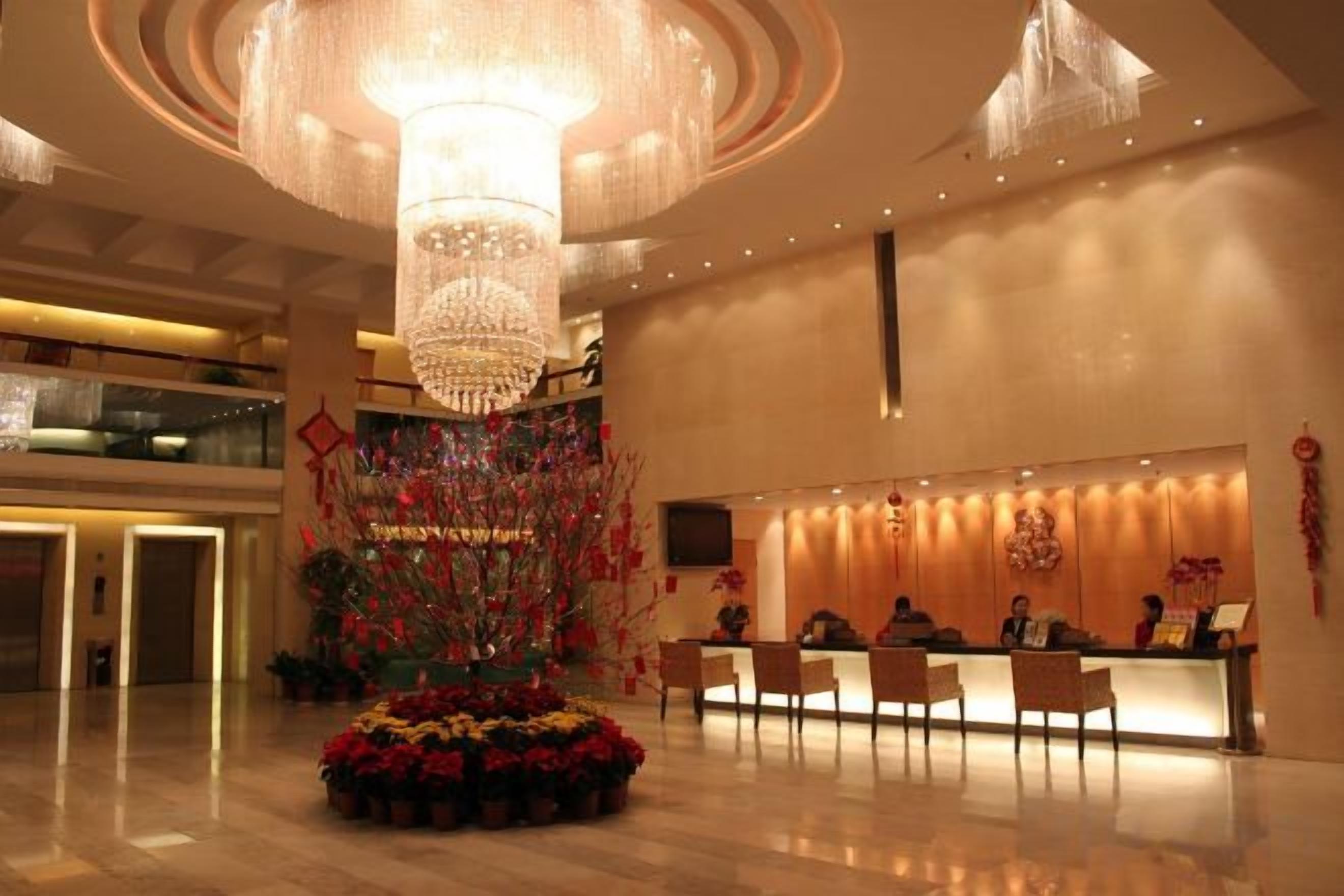Un hall d’hôtel doté d’un grand lustre, d’un comptoir de réception et d’une composition florale décorative.