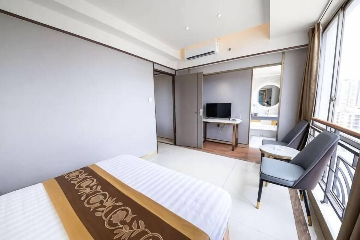 Habitación de hotel con cama, escritorio, televisor y balcón con una silla.
