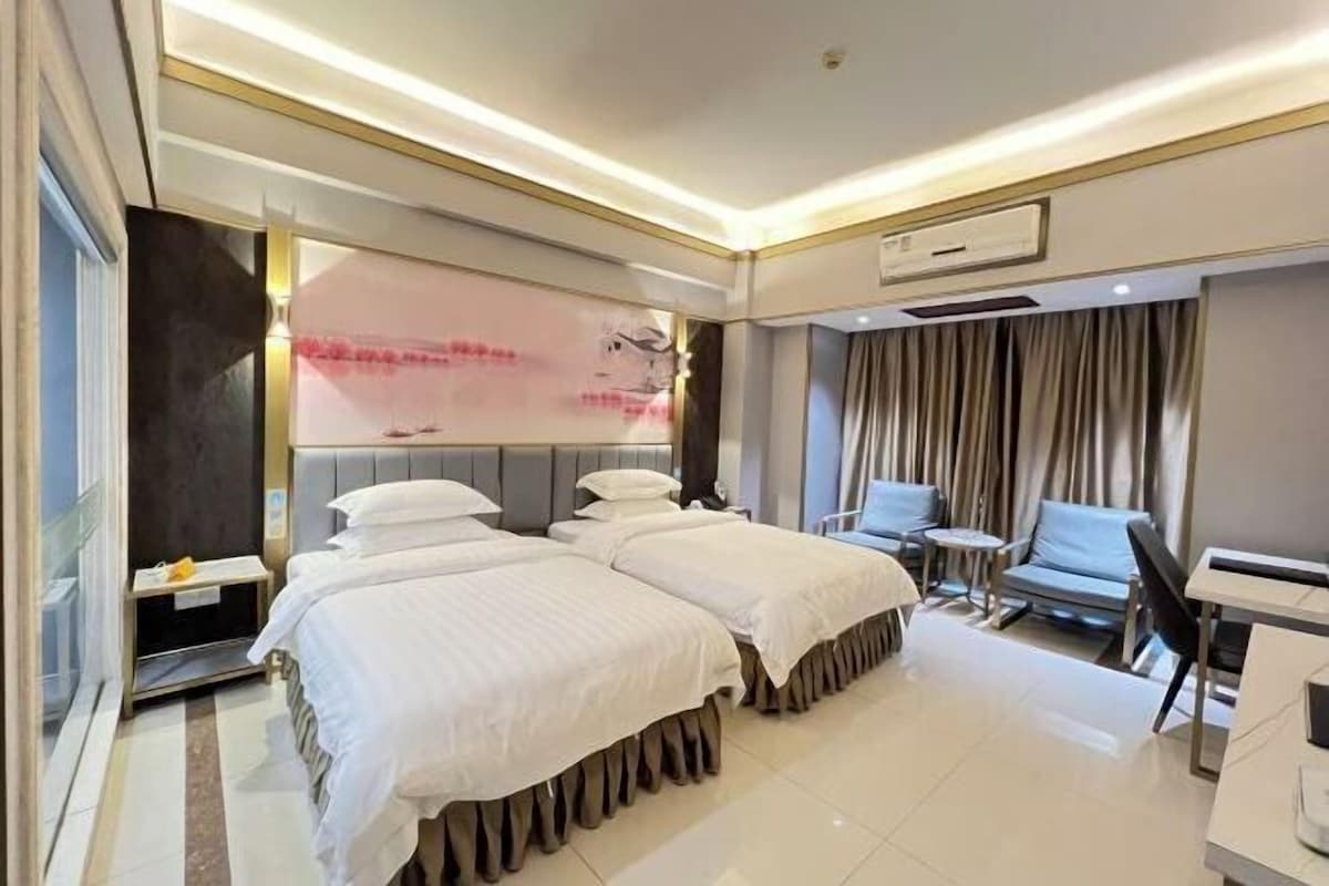 Een hotelkamer met twee bedden, een tafeltje, een stoel en een groot raam met gordijnen.