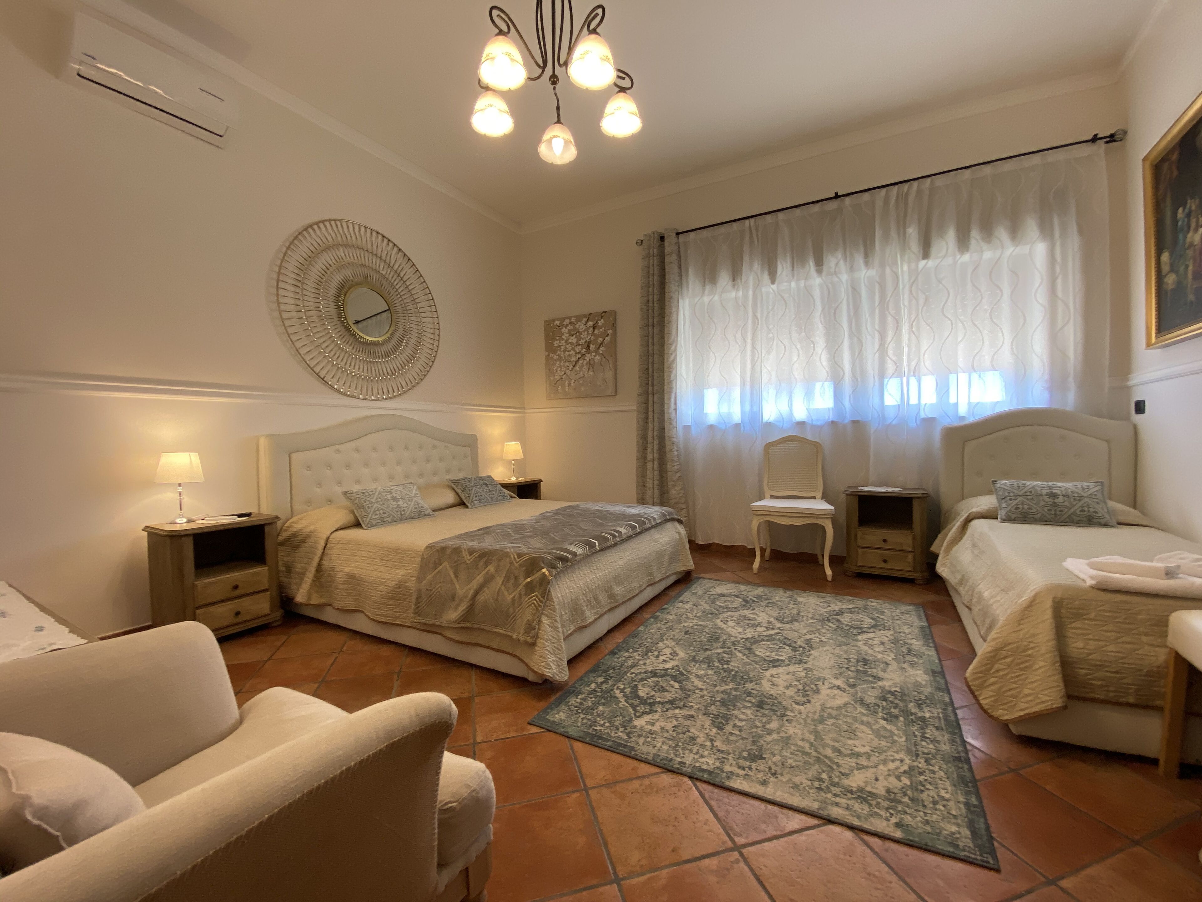 A bedroom with a large bed, two bedside tables, a chair, a small table, and a decorative mirror.