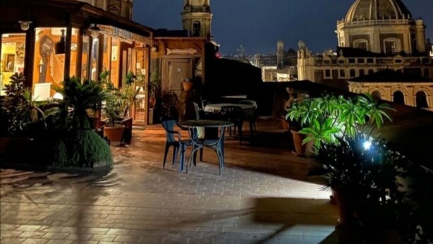 A courtyard with a dining area, potted plants, and two illuminated domes in the background. - San Placido Inn (Catania)