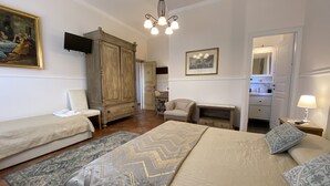 A bedroom with a bed, a chair, a wardrobe, a desk, a mirror, and a television. - San Placido Inn (Catania)