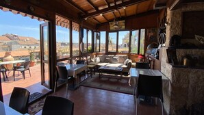 A spacious patio with a wooden ceiling, large windows offering a view of the surrounding landscape, and a variety of seating arrangements including a sofa and tables. - San Placido Inn (Catania)