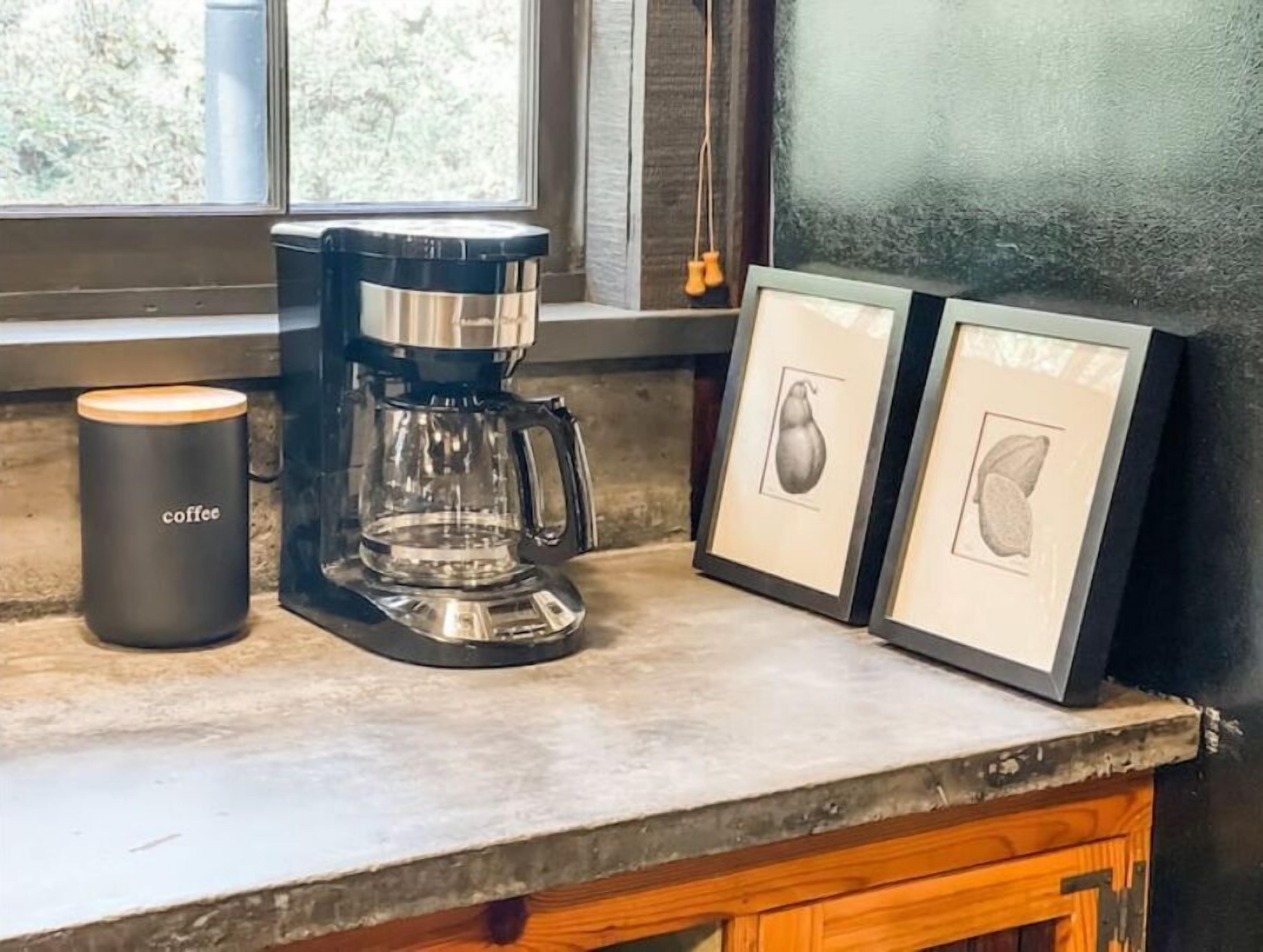 Une machine à café, une bougie étiquetée « café » et deux photos encadrées sur un plan de travail de cuisine.