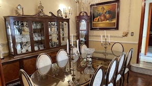 A formal dining room with a glass-top table, ornate chairs, a wooden sideboard with glassware, a grandfather clock, and a framed painting. - Luxurious Boutique Palace in the heart of Condesa (Ciudad de México)