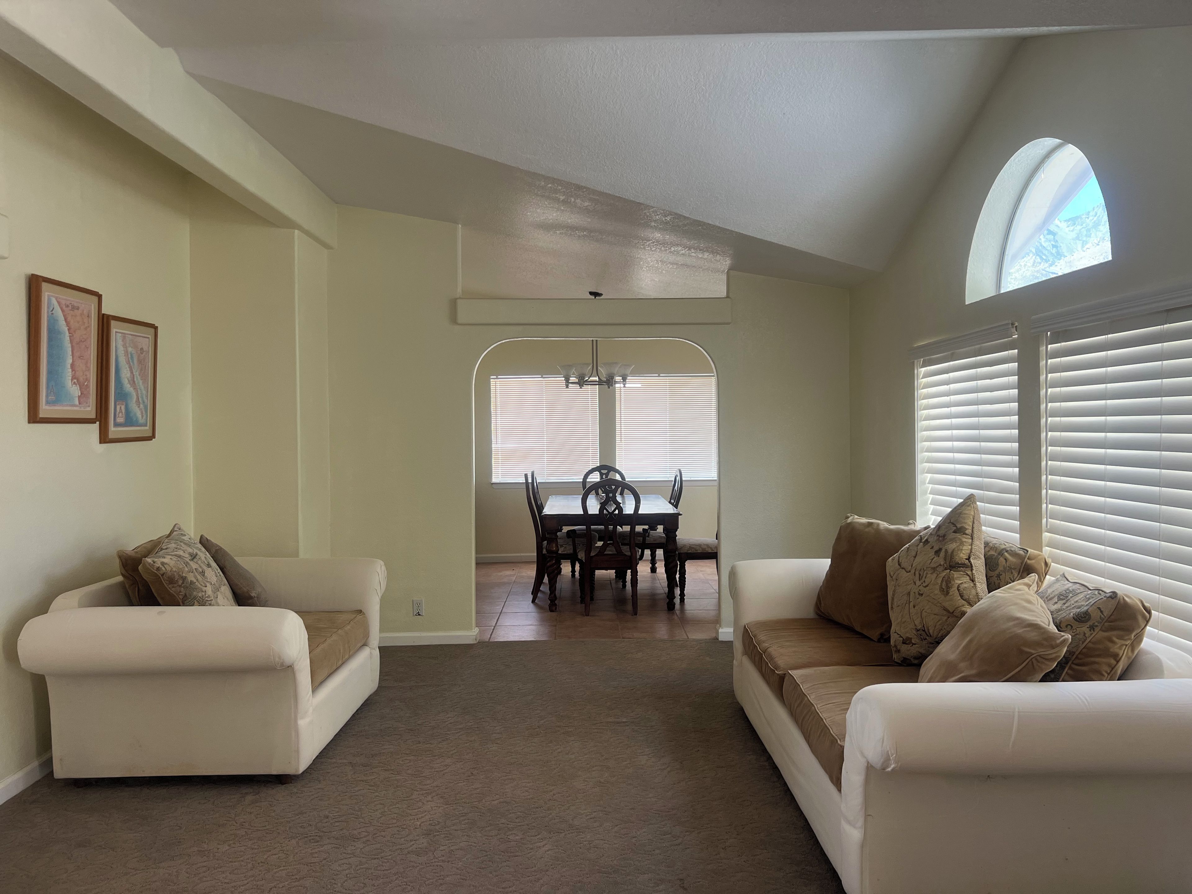 A living room with two white sofas, a dining table with chairs, and a large arched window.