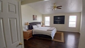 Een slaapkamer met een bed, nachtkastjes, een plafondventilator en kunstwerken aan de muren.