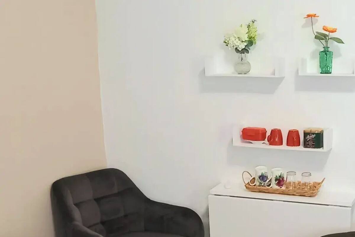 A modern room with a dark grey upholstered armchair, a white desk with shelves holding decorative items and a tray of mugs.