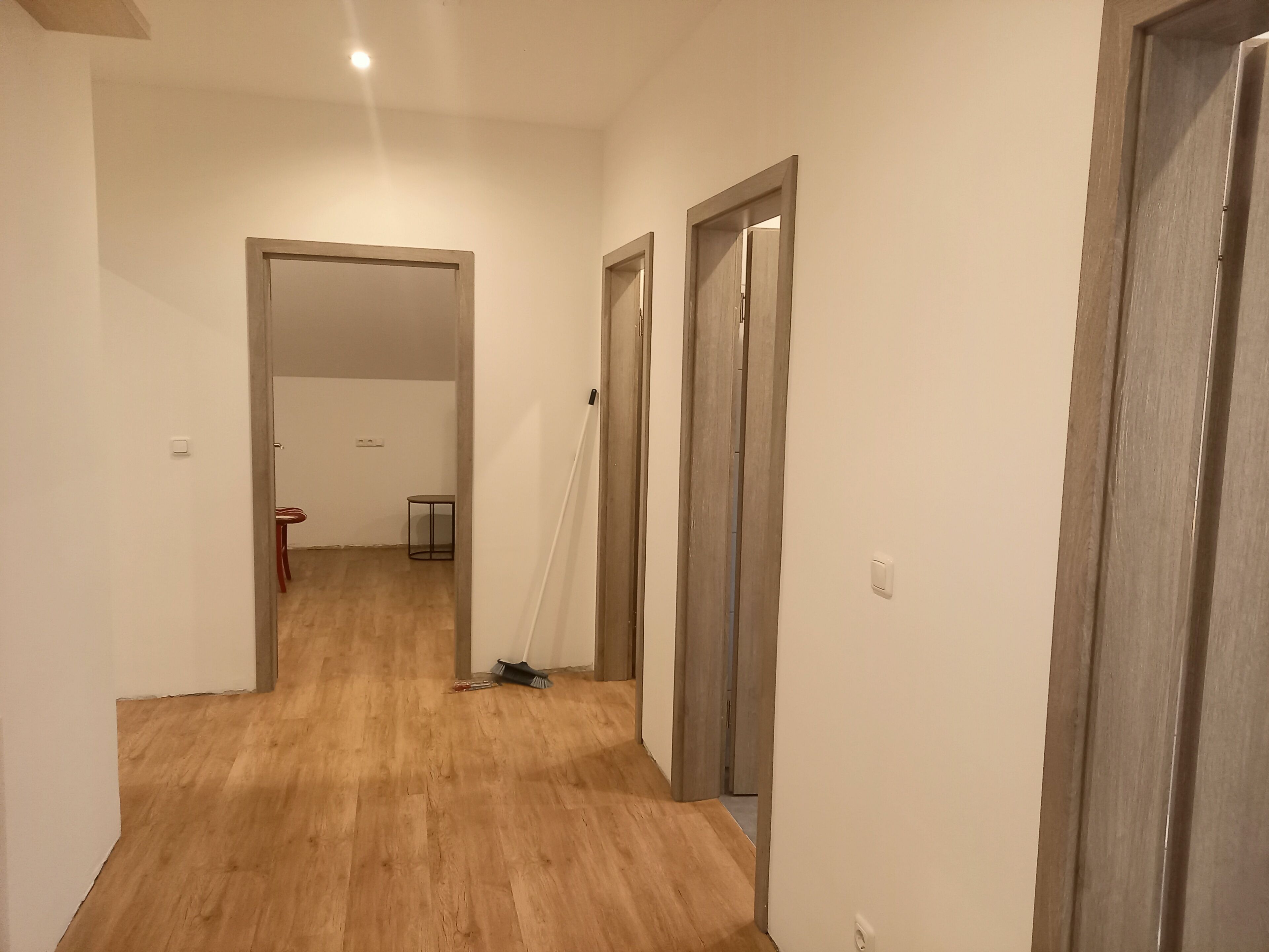 A hallway with wooden flooring, white walls, and a door leading to another room.