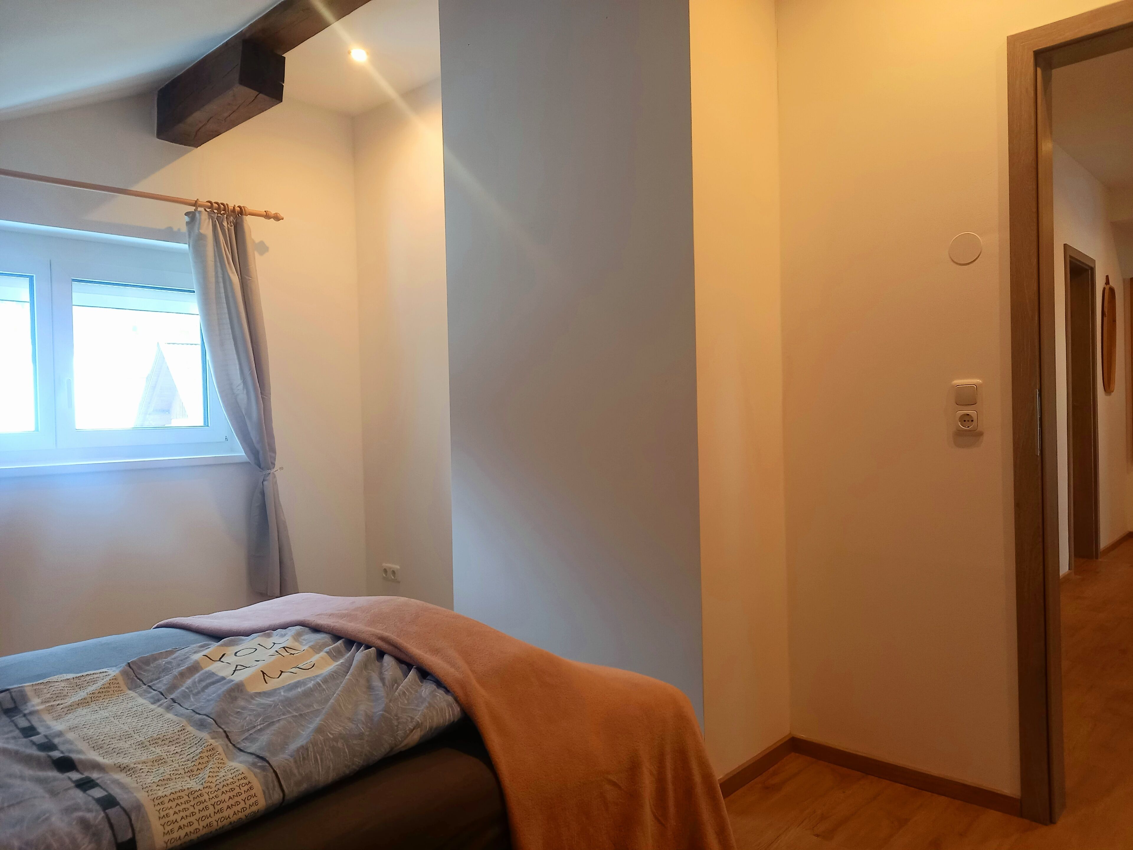 Ein Schlafzimmer mit Bett, einem Fenster mit Vorhängen, einer Tür und einer Steckdose.