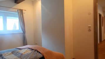 Ein Schlafzimmer mit Bett, einem Fenster mit Vorhängen, einer Tür und einer Steckdose.