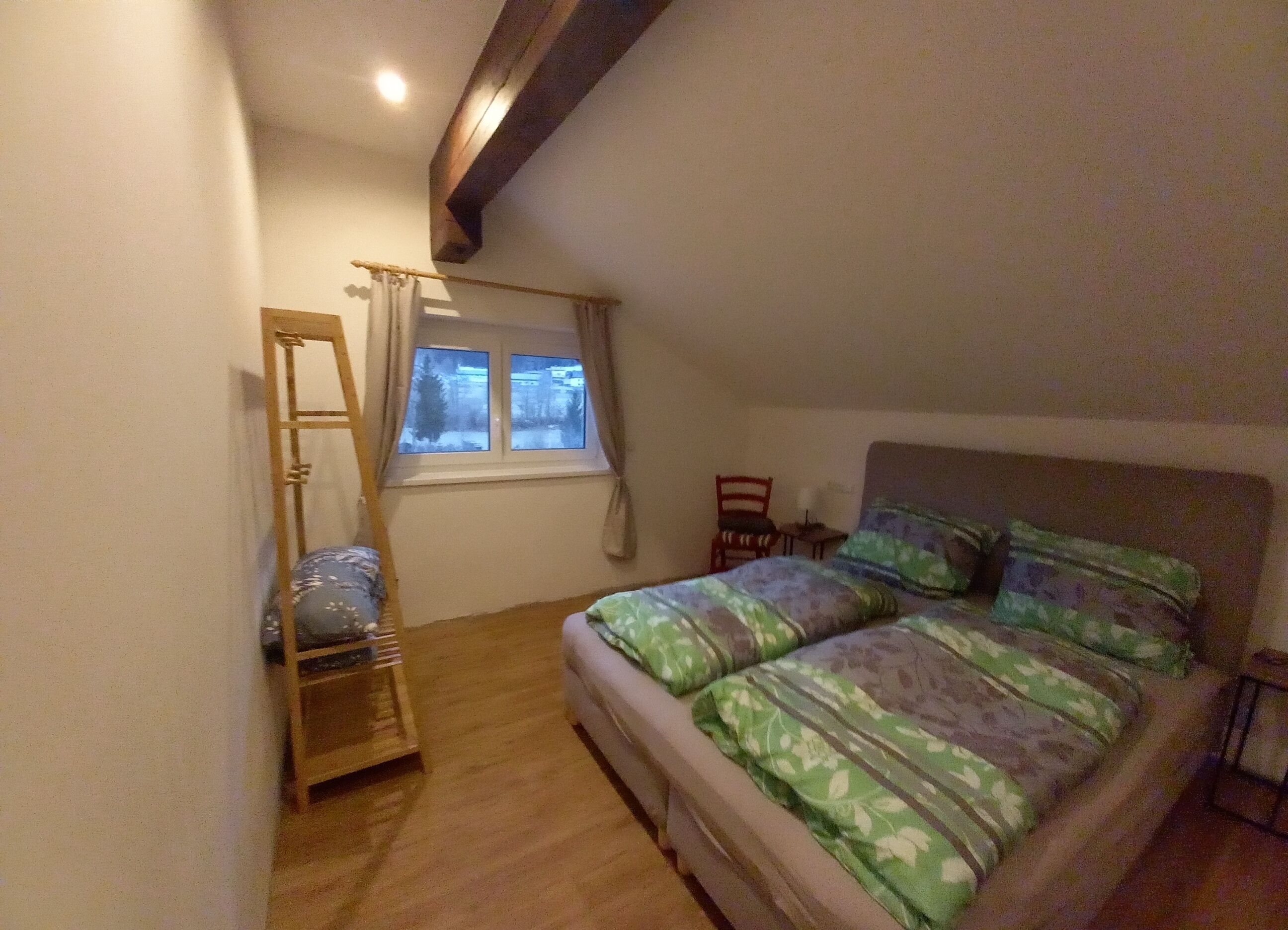 Un dormitorio con una cama, ventana, silla y escalera de madera.