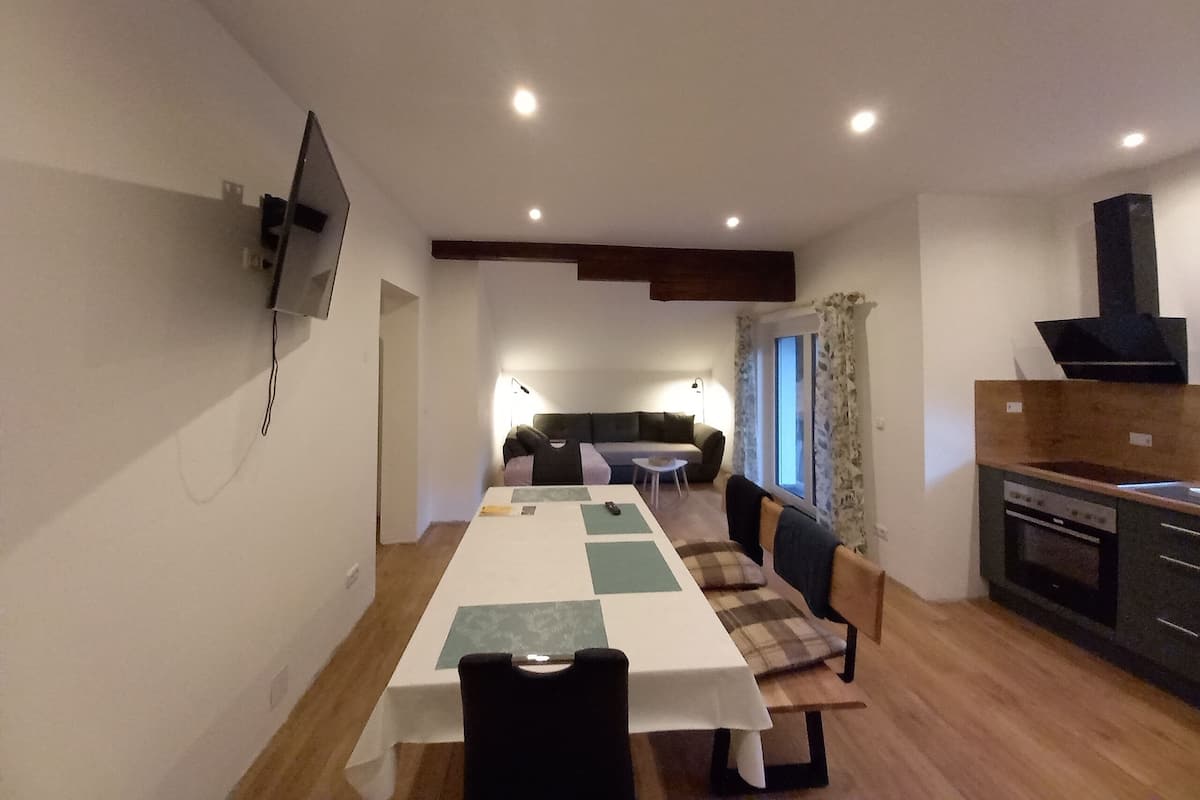 A dining area with a table set for four, a sofa, and a kitchen area with a stove.