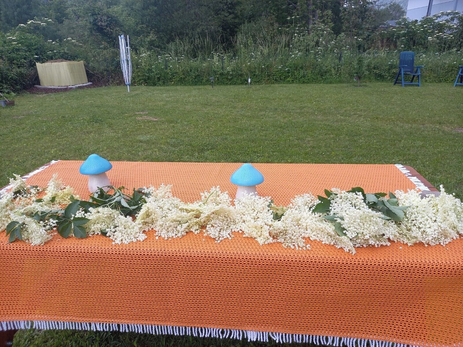 A table with a crocheted orange tablecloth, two blue mushroom-shaped candle holders, and white flowers.