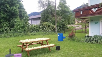Et picnicbord med blomster, en blå genbrugsbeholder og et hus med en træbalkon.