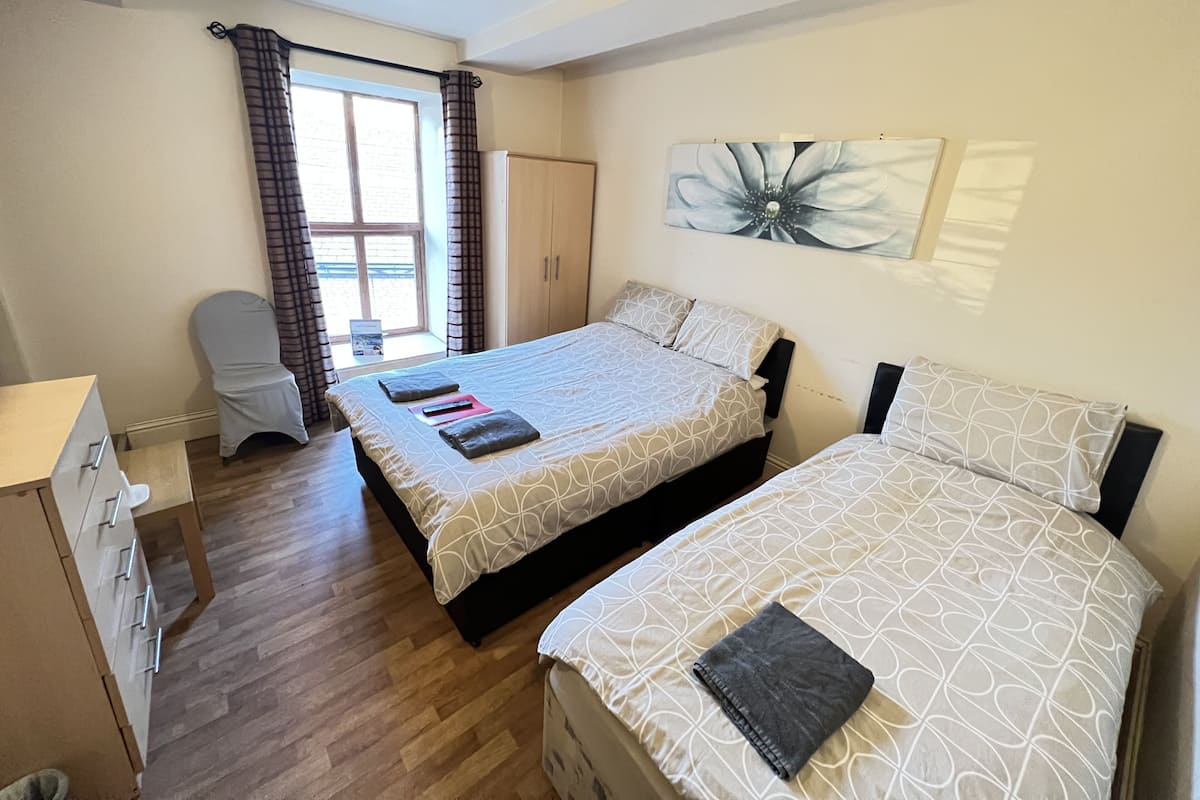 A bedroom with two beds, a desk, a chair, a wardrobe, and a window with curtains.