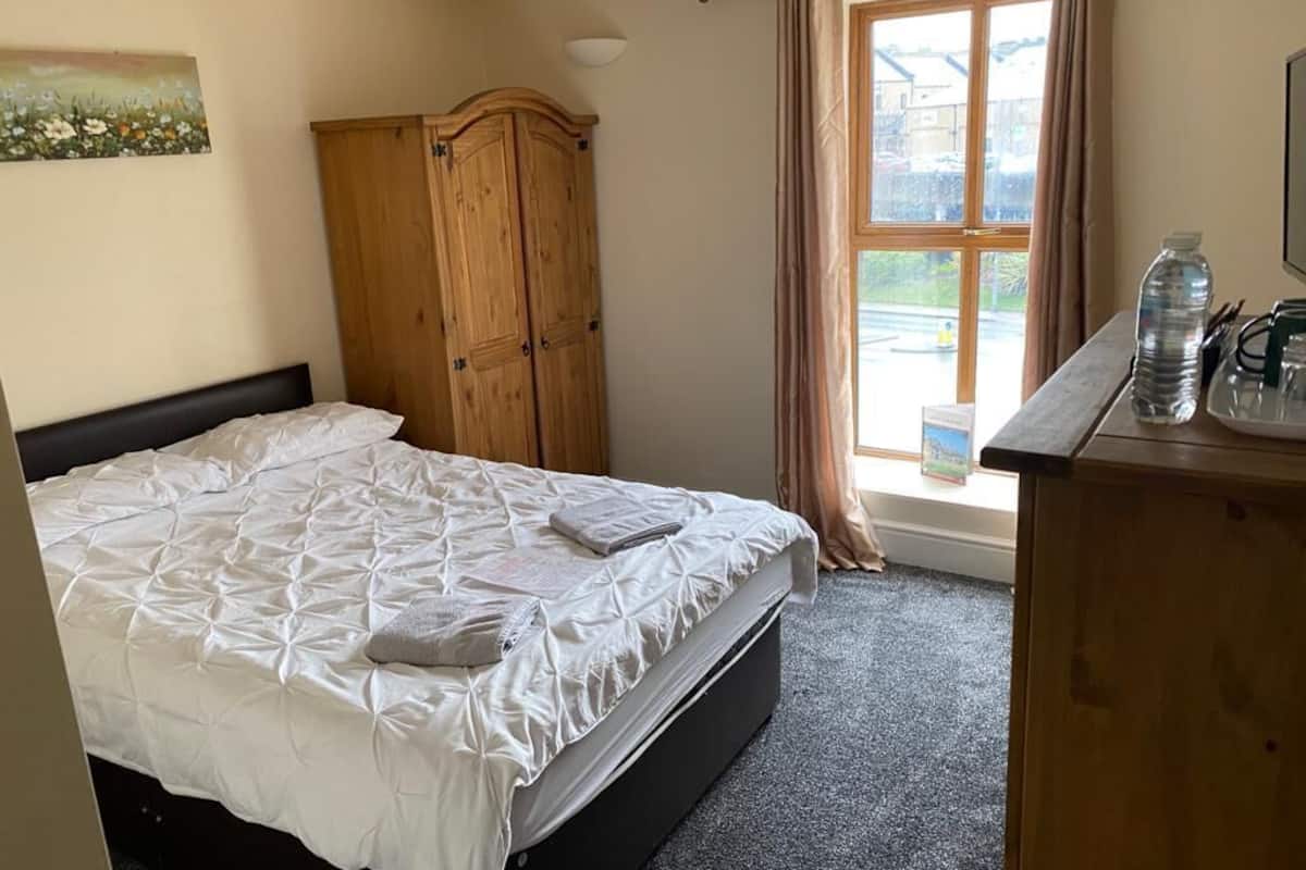 A bedroom with a bed, a wooden wardrobe, a window with curtains, and a desk with a water bottle.