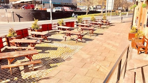 An outdoor seating area with wooden benches and tables, a paved walkway, and a building in the background. - The old post office hotel (Halifax)