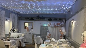 A banquet hall with tables set for a formal event, featuring white tablecloths and chairs, a ceiling with decorative lights, and a backdrop of balloons. - The old post office hotel (Halifax)