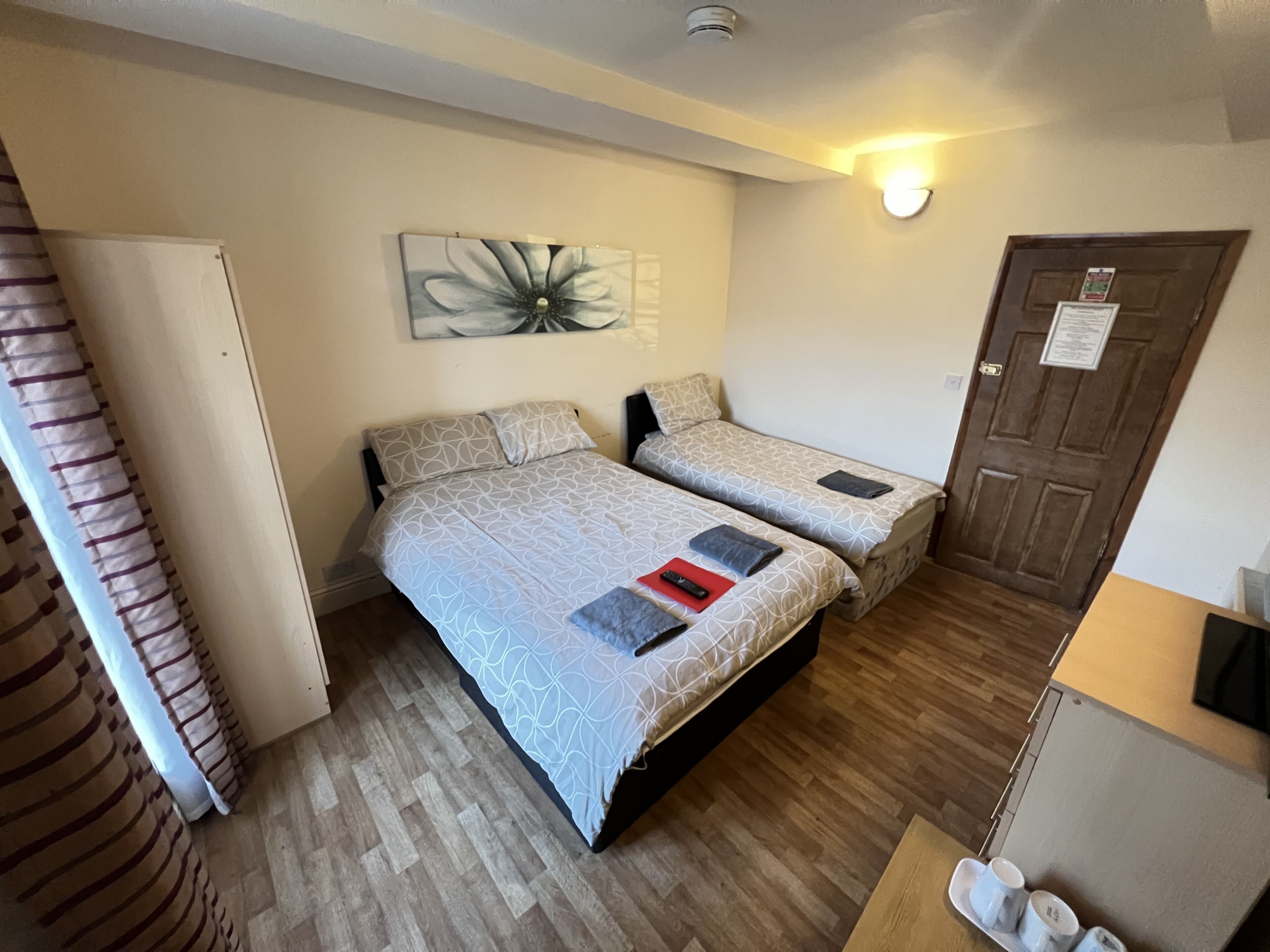 Una habitación con dos camas, piso de madera, una lámpara fijada a la pared y una puerta con un letrero.