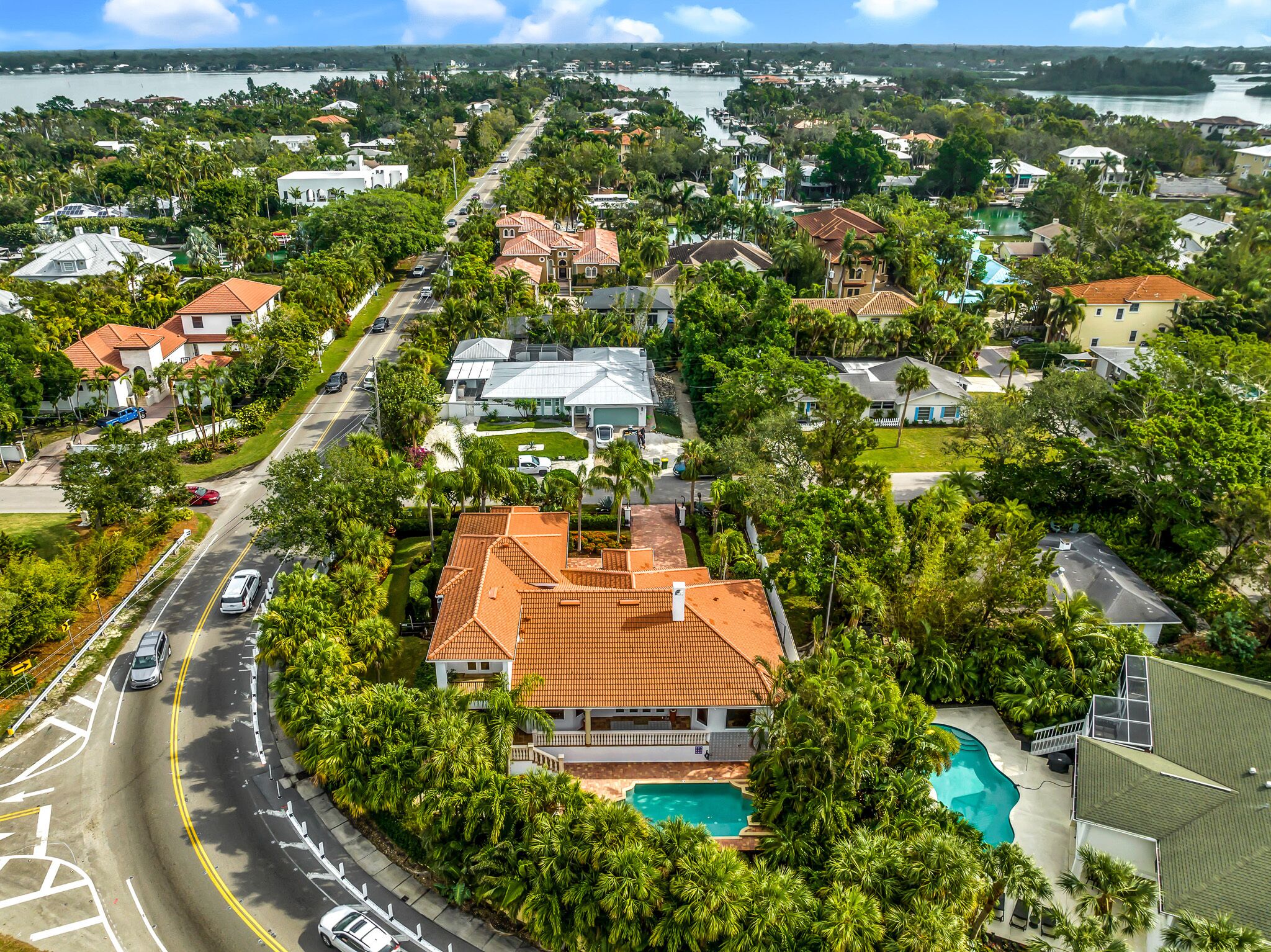 An aerial view of a residential area with houses, a road, and a large body of water in the background.