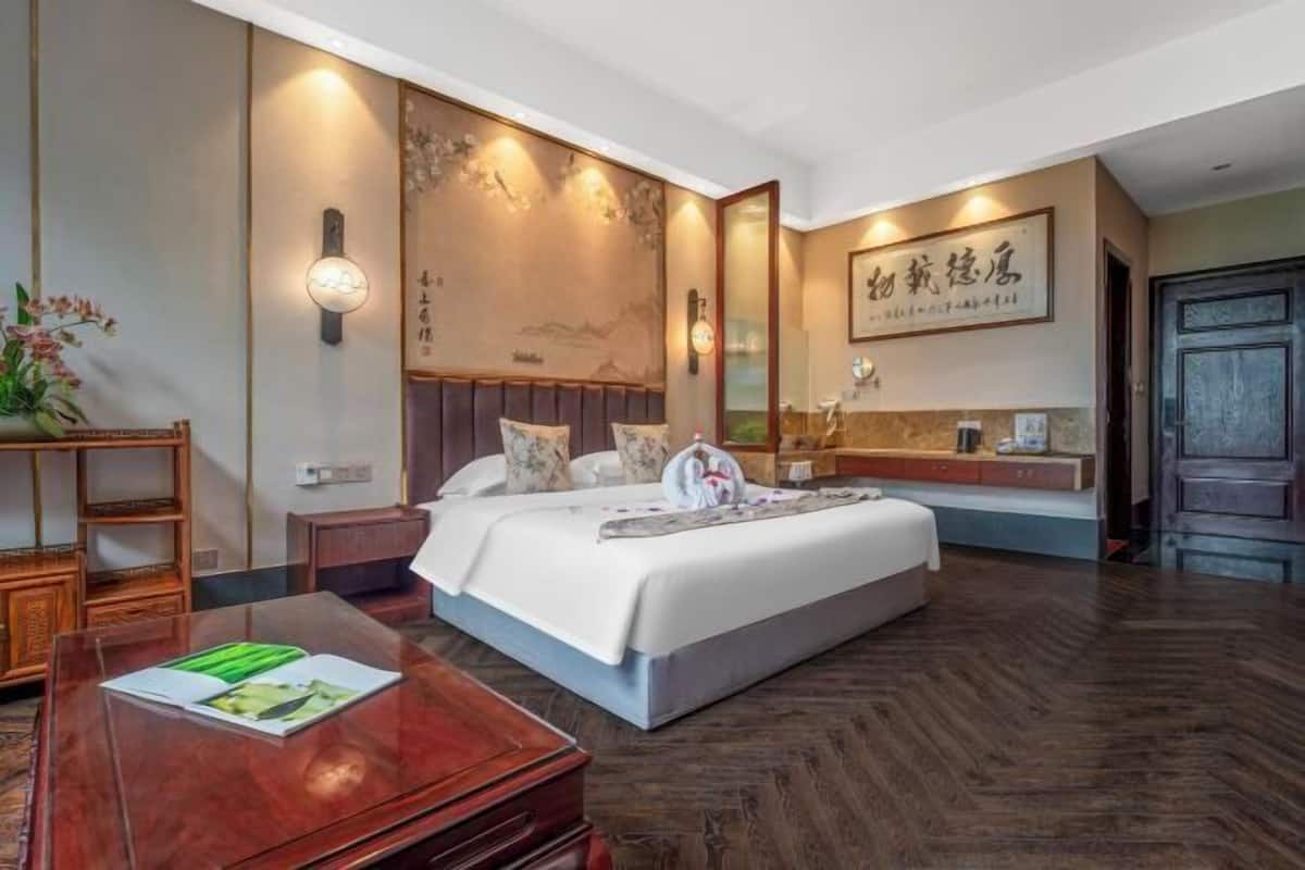 Una habitación de hotel con una cama, mesita de noche, luz en la pared y suelo de madera.
