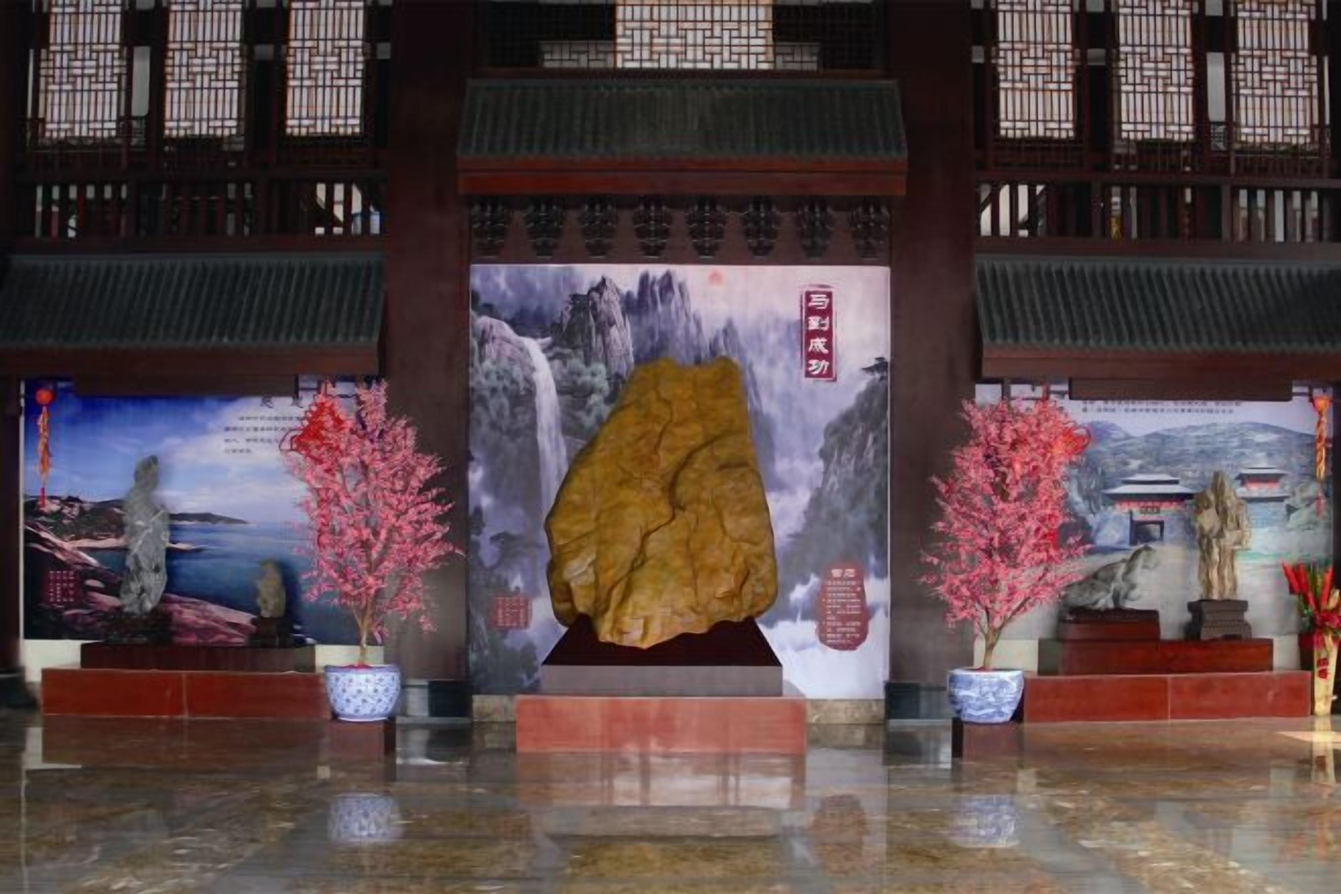 Ein traditionelles chinesisches architektonisches Interieur mit einer großen Felsformation, zwei Zimmerpflanzen und einem Gemälde eines Wasserfalls.