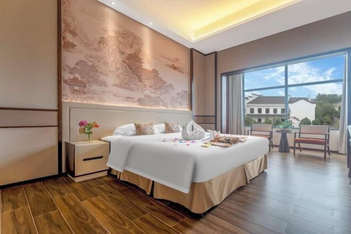 Habitación de hotel moderna con una cama grande, una mesita de noche, un mural en la pared y vistas al exterior.