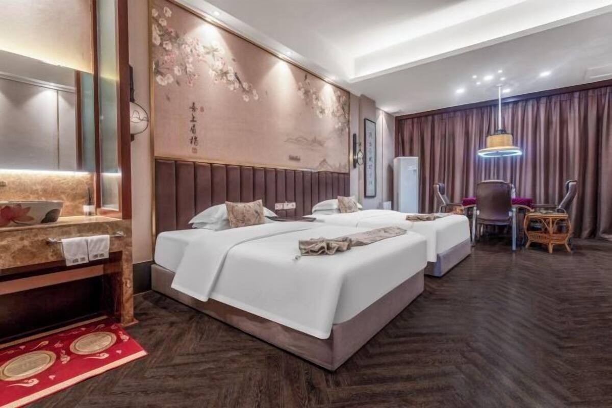 Habitación de hotel con dos camas, un escritorio, una silla, un espejo, una pared decorada con obras de arte y una alfombra roja estampada.