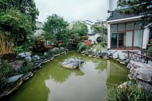 Um jardim tranquilo com um lago, rodeado por pedras e diversas plantas.
