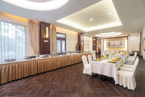 Une salle de banquet avec une longue table, des chaises et un buffet.