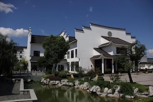 Um edifício moderno com um lago, rodeado por vegetação e um céu limpo.